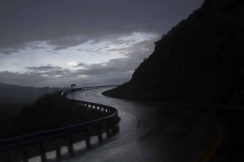 A wet road curving along the east side of Horsetooth Reservoir under a dark sky