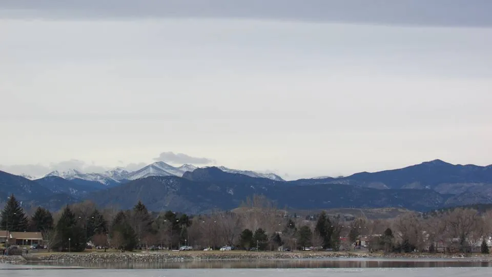 Snow-capped peaks of the Front Range behind the trees and houses of Lake Loveland