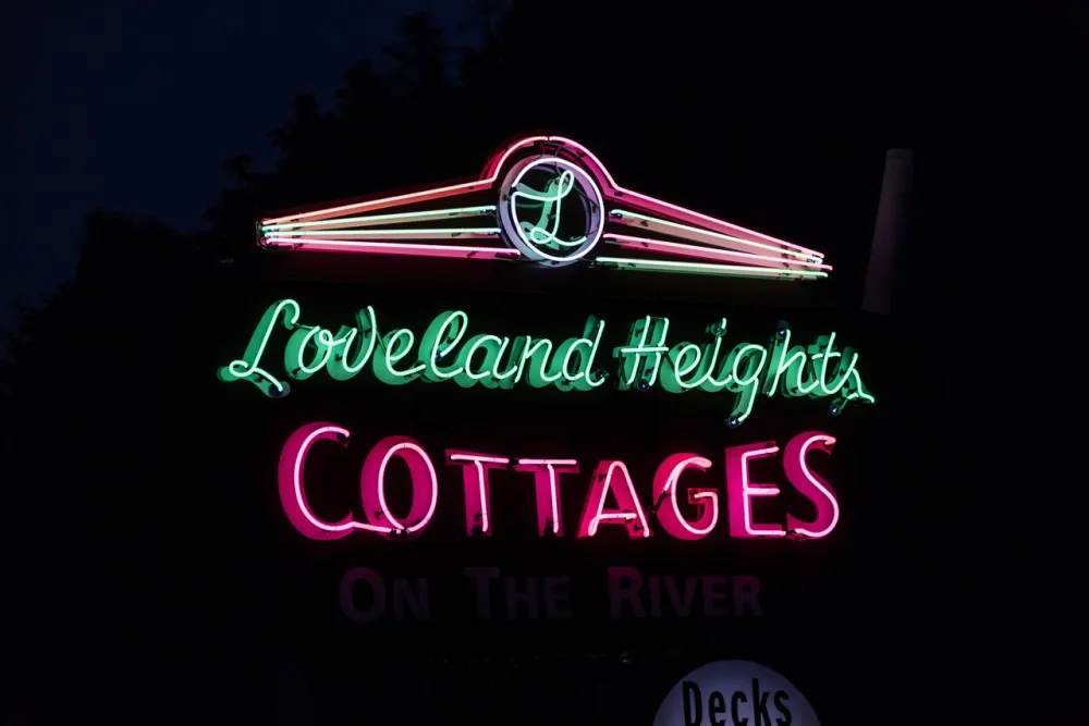 A pink and green neon sign reading Loveland Heights Cottages, On the River, at night